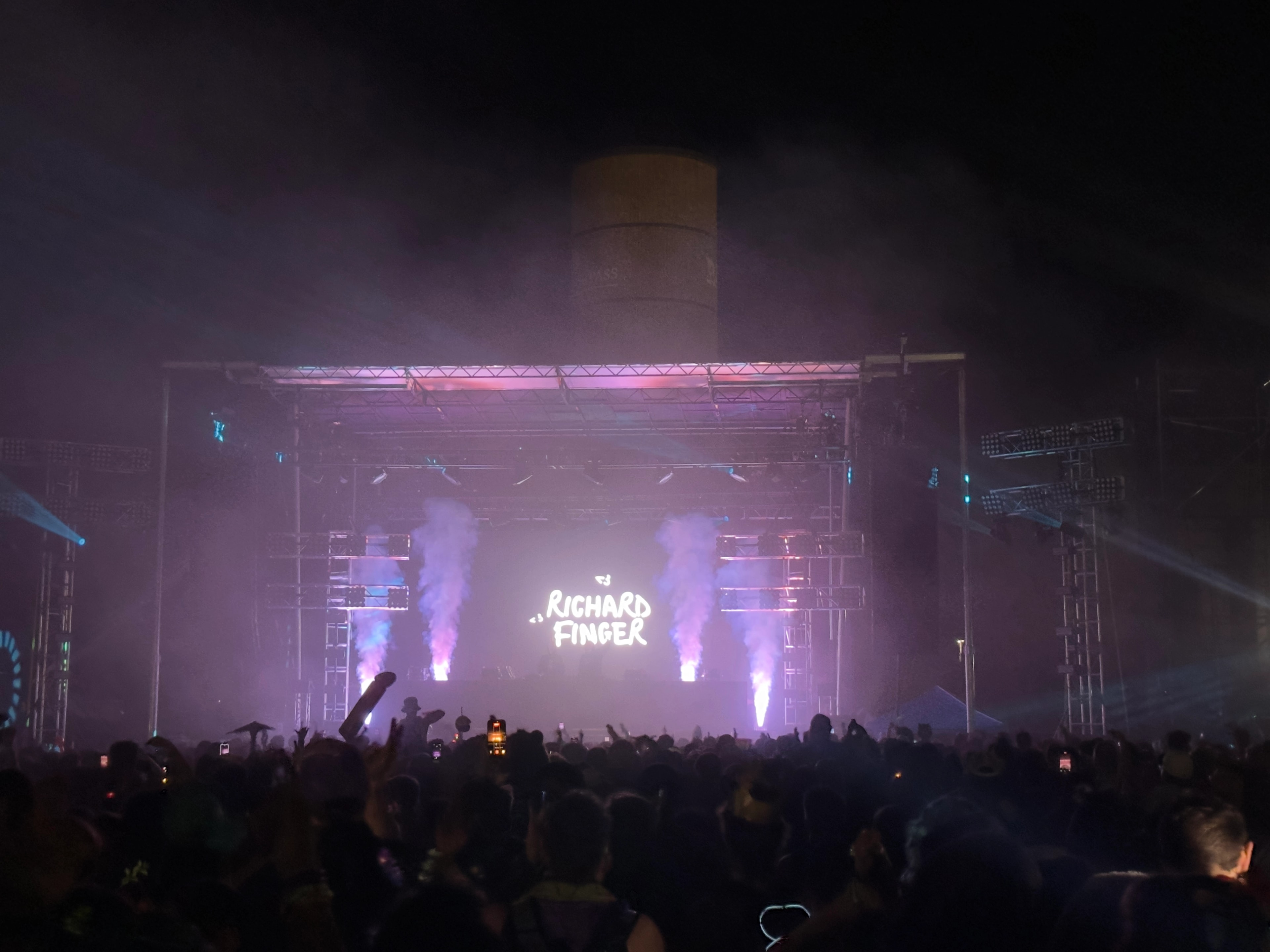 Richard Finger performing on stage with fog machines and purple lighting, crowd with hands raised